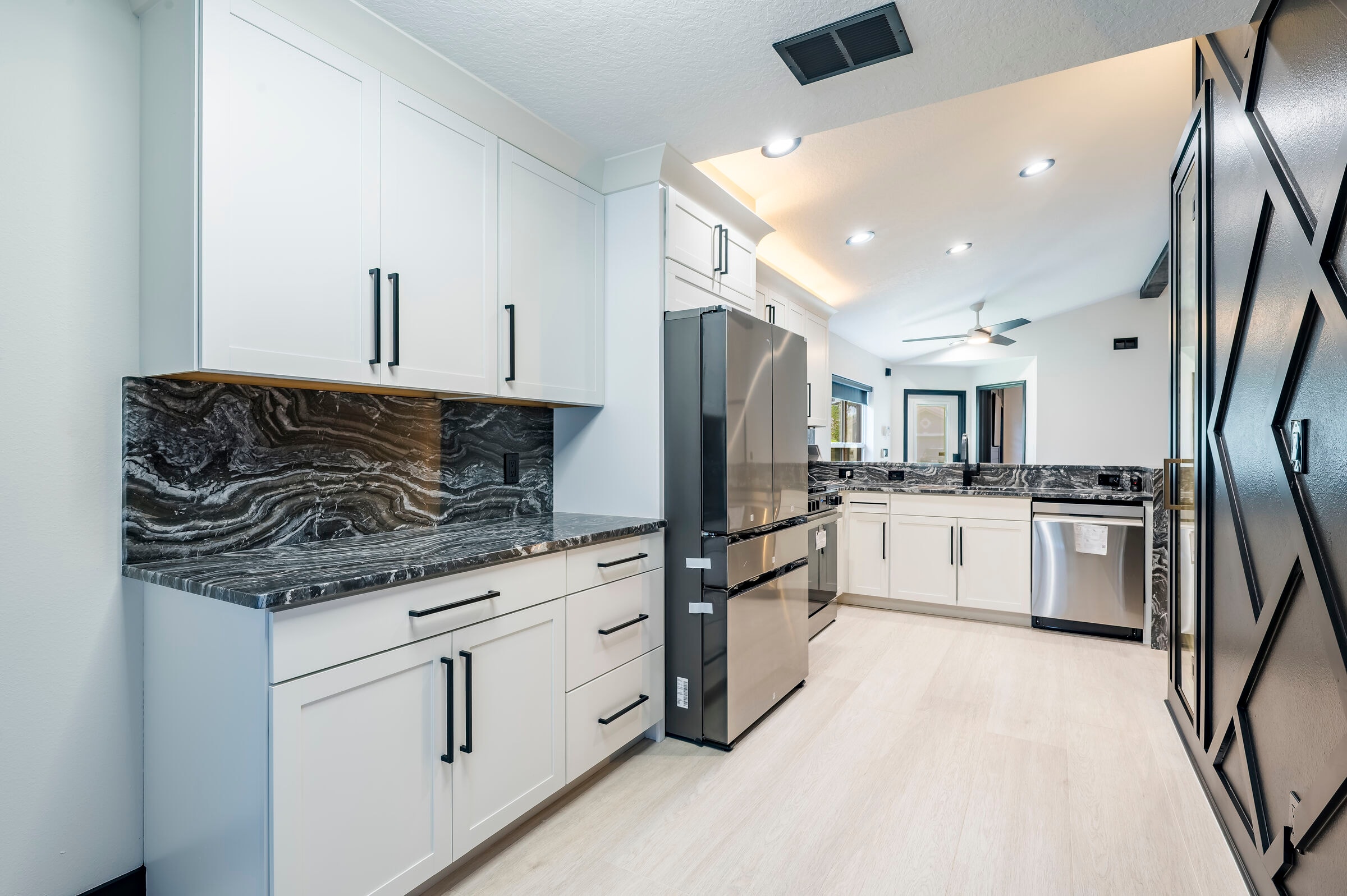 Full kitchen view at 7522 Oxford Garden Circle Apollo Beach — white shaker cabinets, dark marble countertops, stainless appliances, and black exposed beams