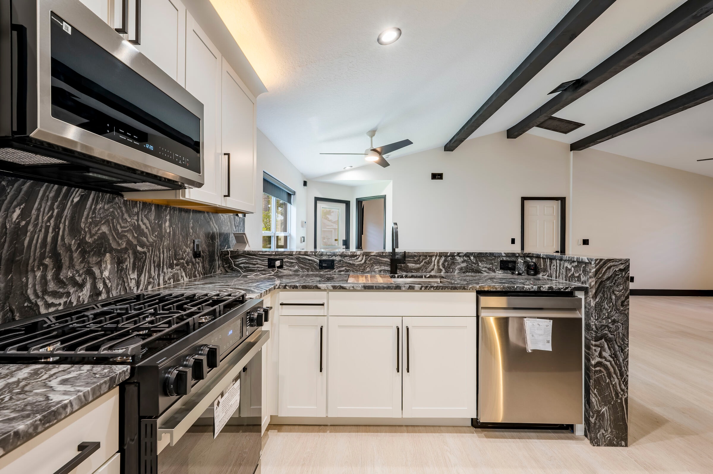 Kitchen range detail at 7522 Oxford Garden Circle Apollo Beach Florida — gas range, over-range microwave, dark marble counters, and exposed black beams