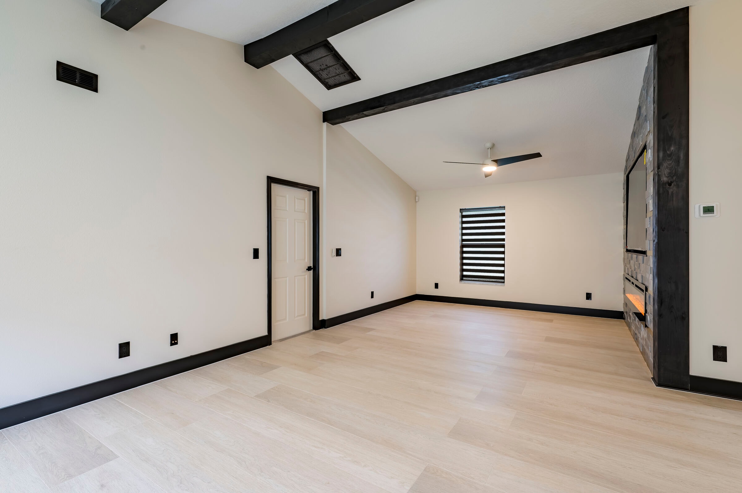 Great room at 7522 Oxford Garden Circle in Apollo Beach — vaulted ceiling with black exposed beams, luxury vinyl plank flooring, and stone fireplace wall