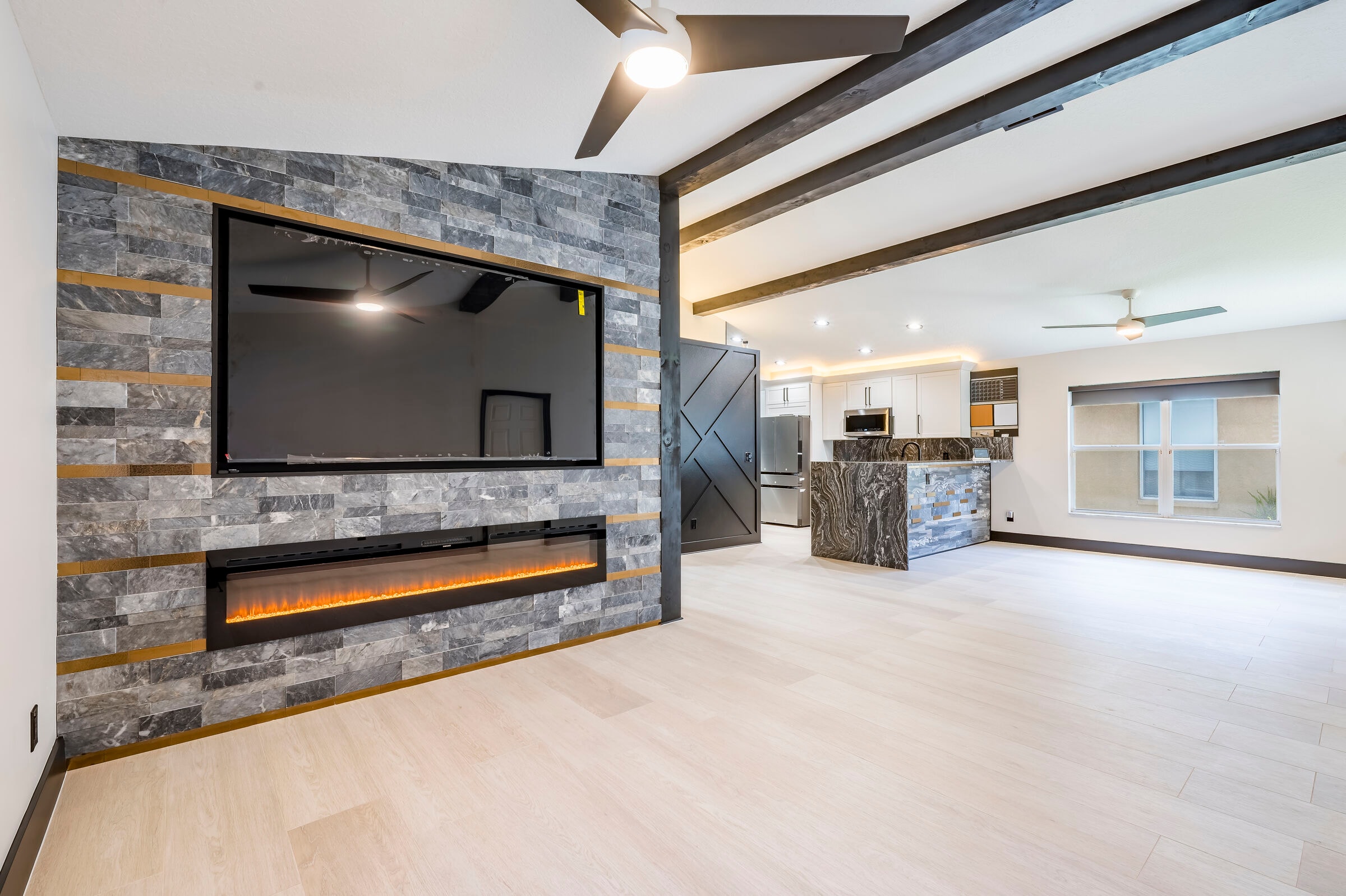 Great room wide view at 7522 Oxford Garden Circle in Apollo Beach Florida — stone fireplace wall, open kitchen beyond, and black exposed beams throughout