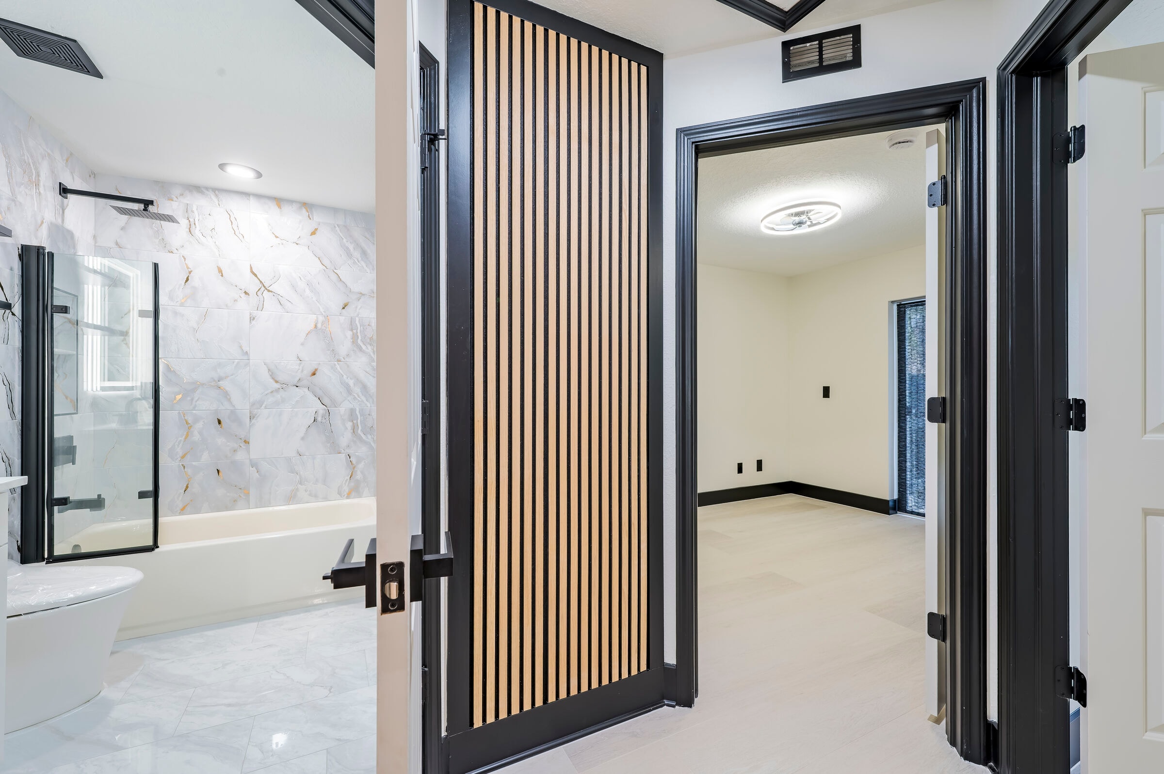 Hallway at 7522 Oxford Garden Circle in Apollo Beach Florida — wood slat barn door, marble guest bathroom visible, and bedroom beyond