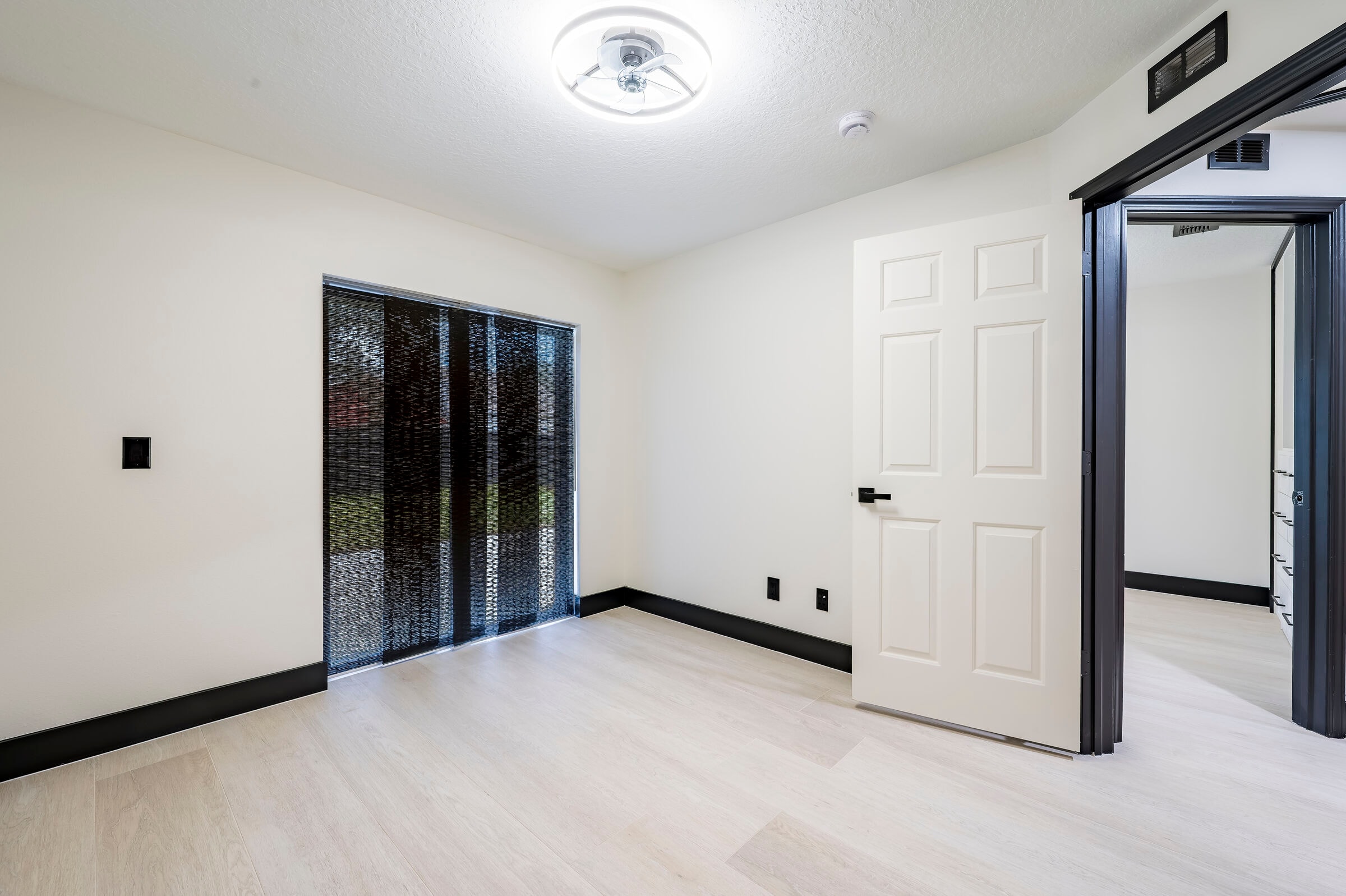 Bedroom at 7522 Oxford Garden Circle in Apollo Beach — sliding glass door with black blinds and open door to hallway