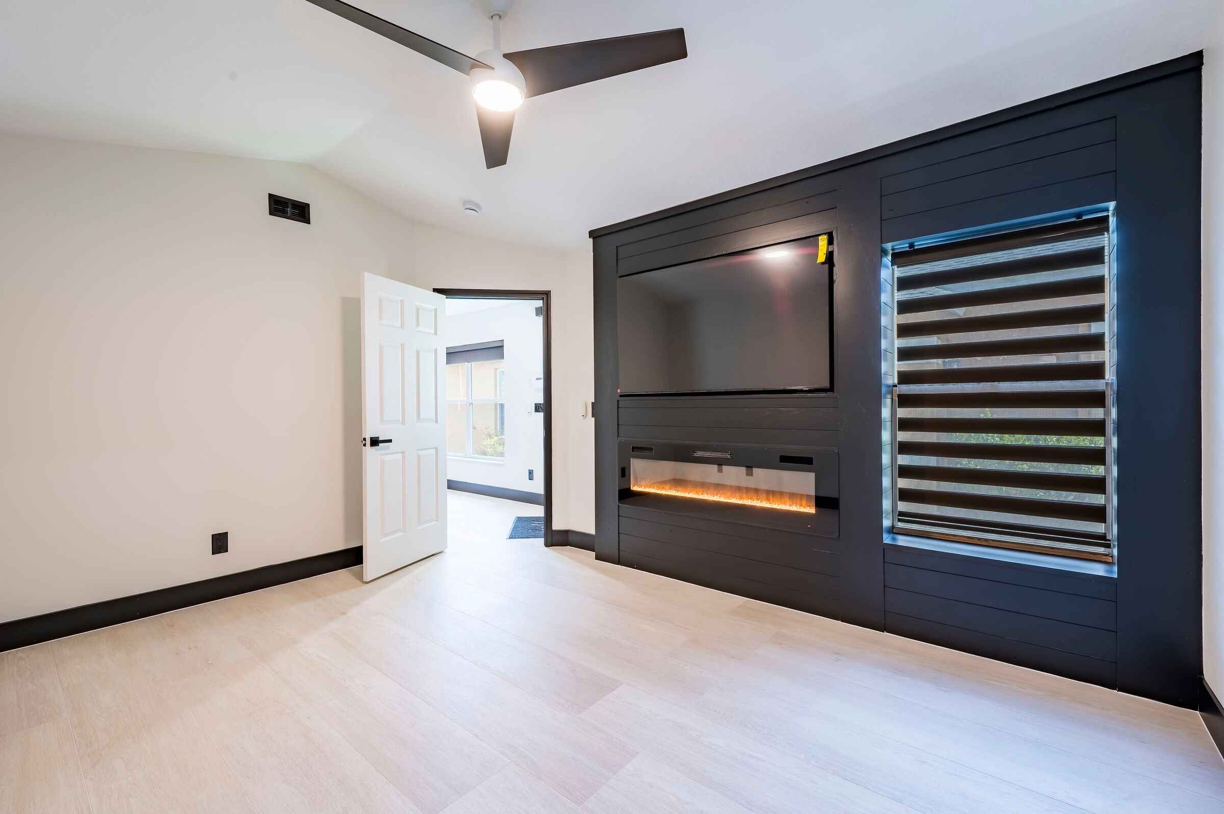 Primary bedroom at 7522 Oxford Garden Circle Apollo Beach Florida — dark shiplap feature wall, linear electric fireplace, smart blinds, and luxury vinyl plank flooring