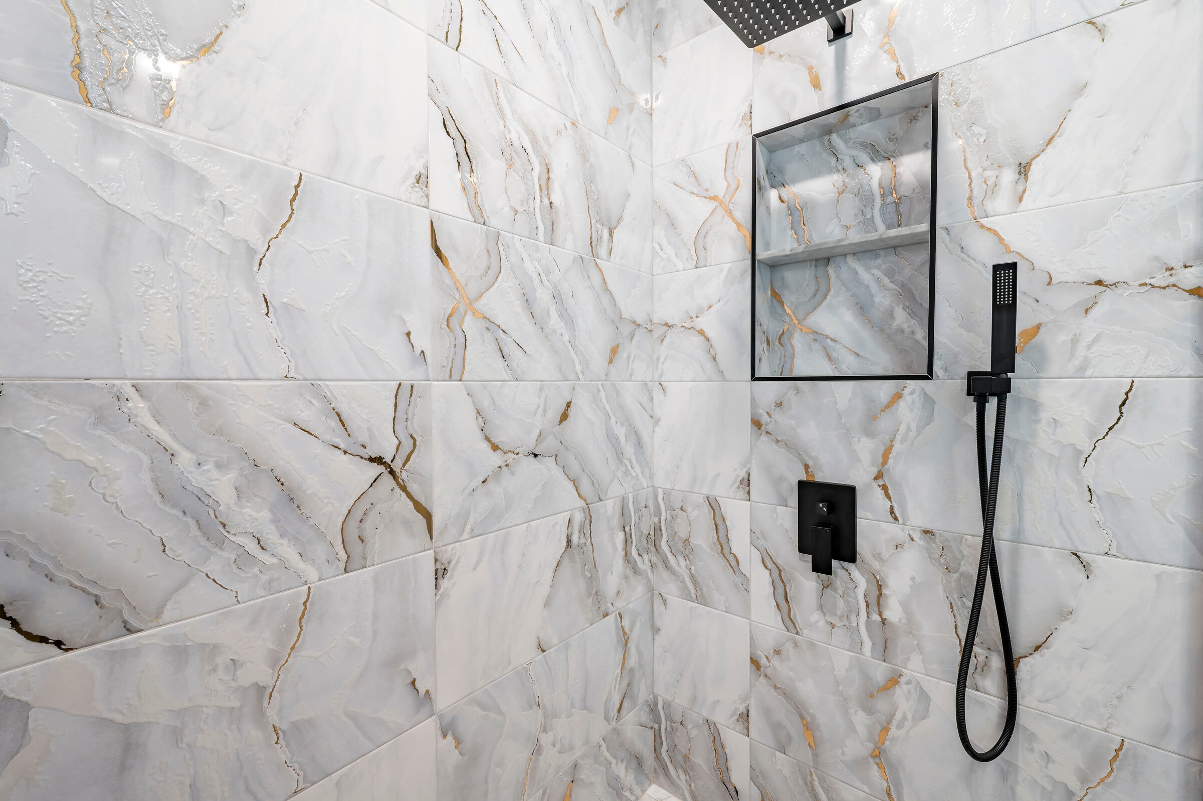 Primary bathroom shower at 7522 Oxford Garden Circle Apollo Beach — floor-to-ceiling gold-veined marble tile, rain head, handheld wand, and built-in niche