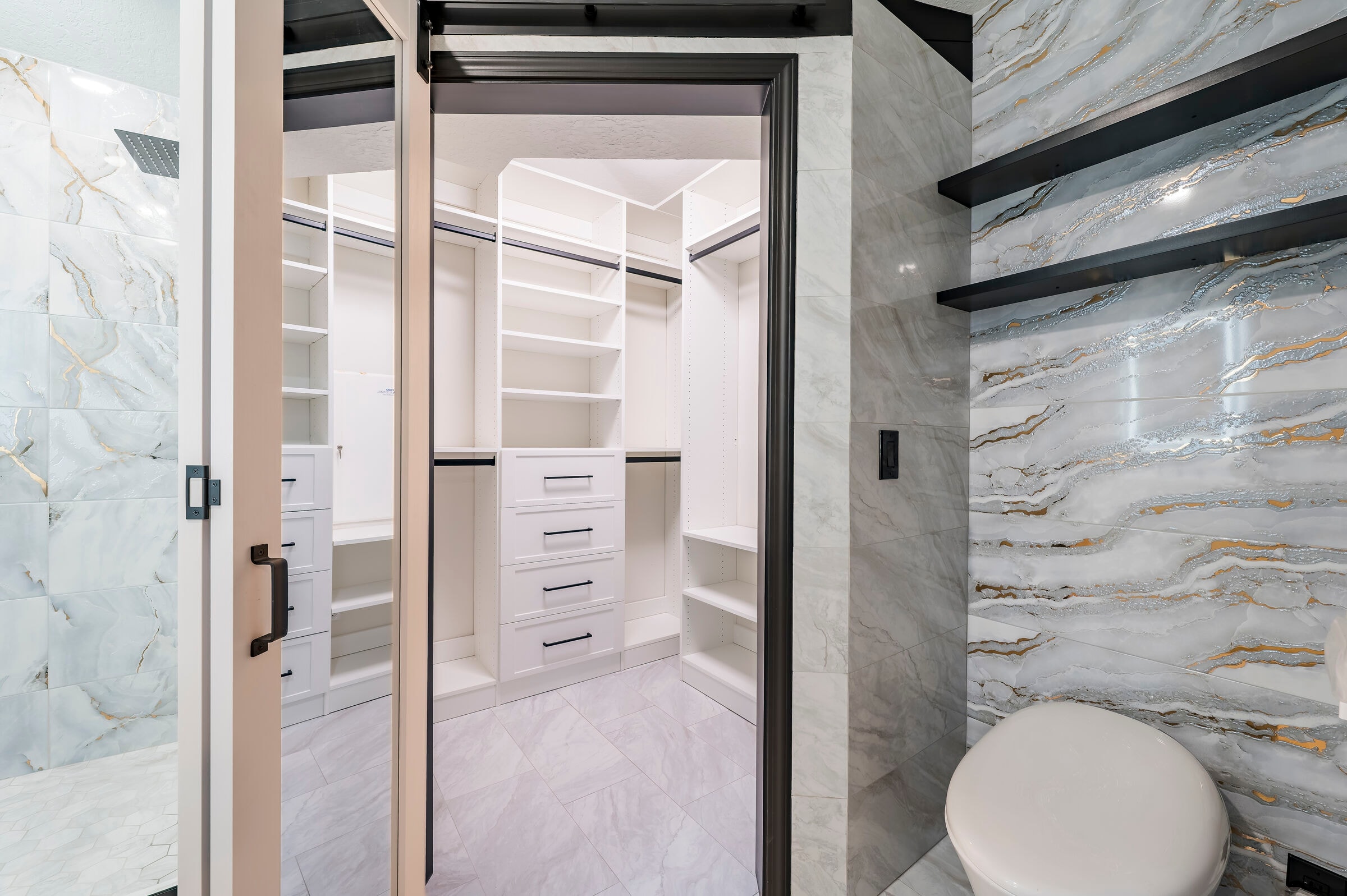 Primary bathroom and walk-in closet at 7522 Oxford Garden Circle in Apollo Beach Florida — marble tile surround and black floating shelves