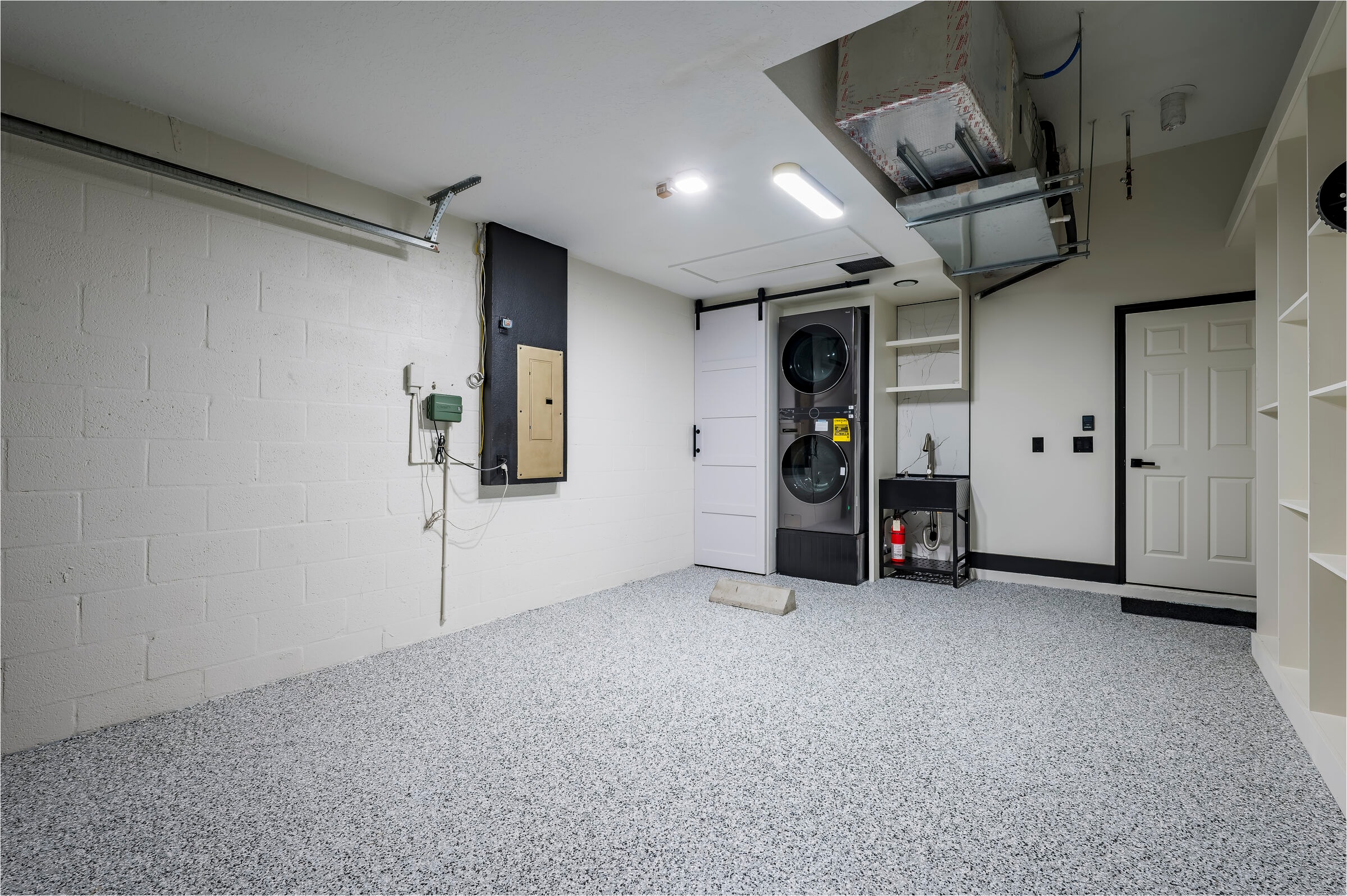 Garage with custom storage and utility sink at 7522 Oxford Garden Circle in Apollo Beach — epoxy floor, stacked washer and dryer, barn door, and utility sink