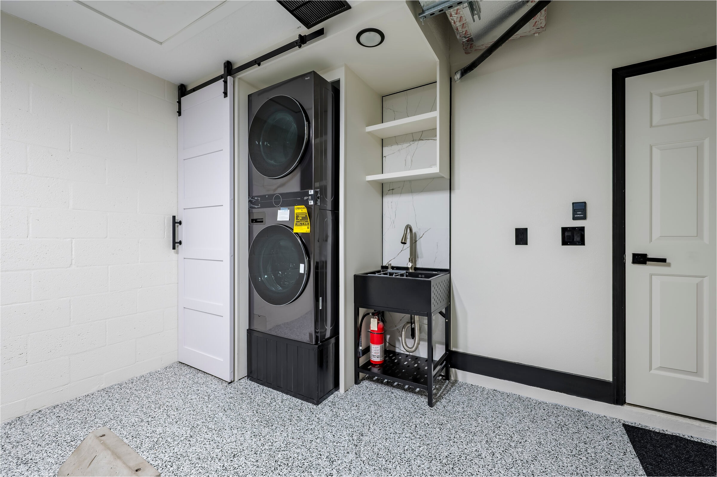 Garage laundry area at 7522 Oxford Garden Circle Apollo Beach Florida — stacked black washer and dryer, white barn door, utility sink, and epoxy flake floor