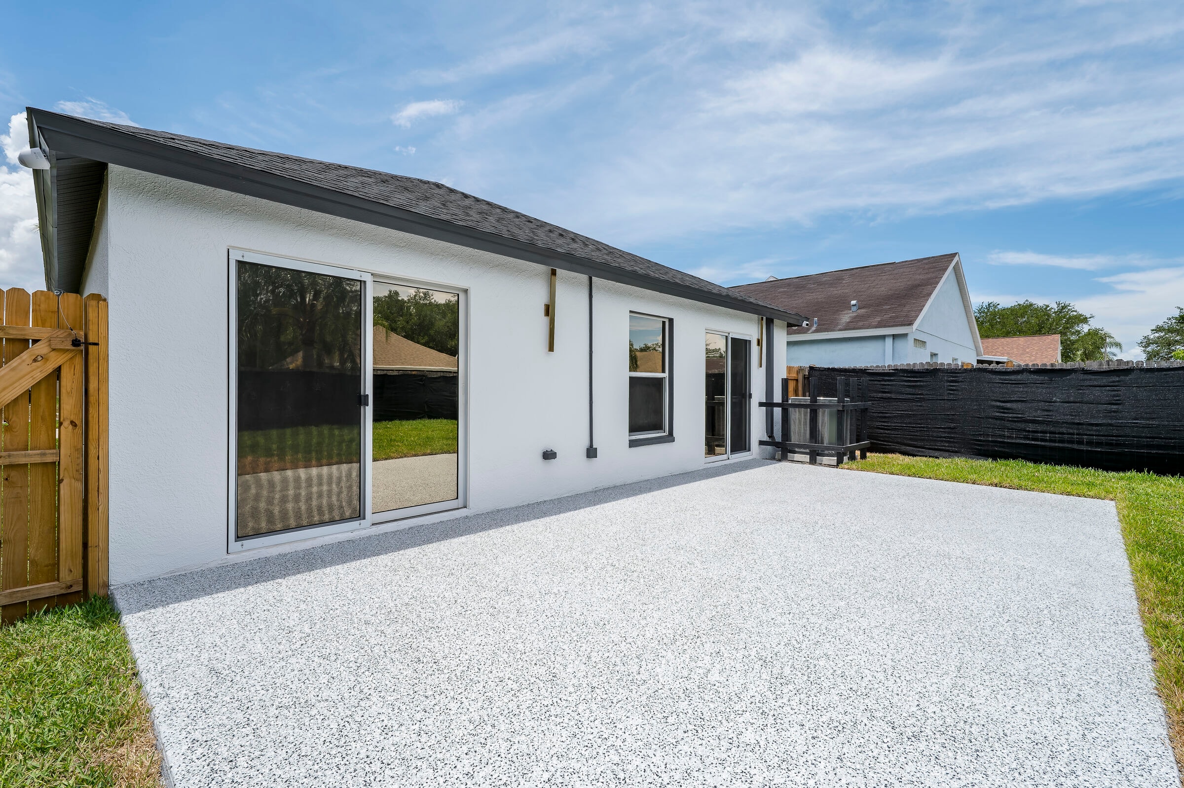 Rear exterior of 7522 Oxford Garden Circle in Apollo Beach Florida — epoxy patio, sliding glass doors, and black privacy fence