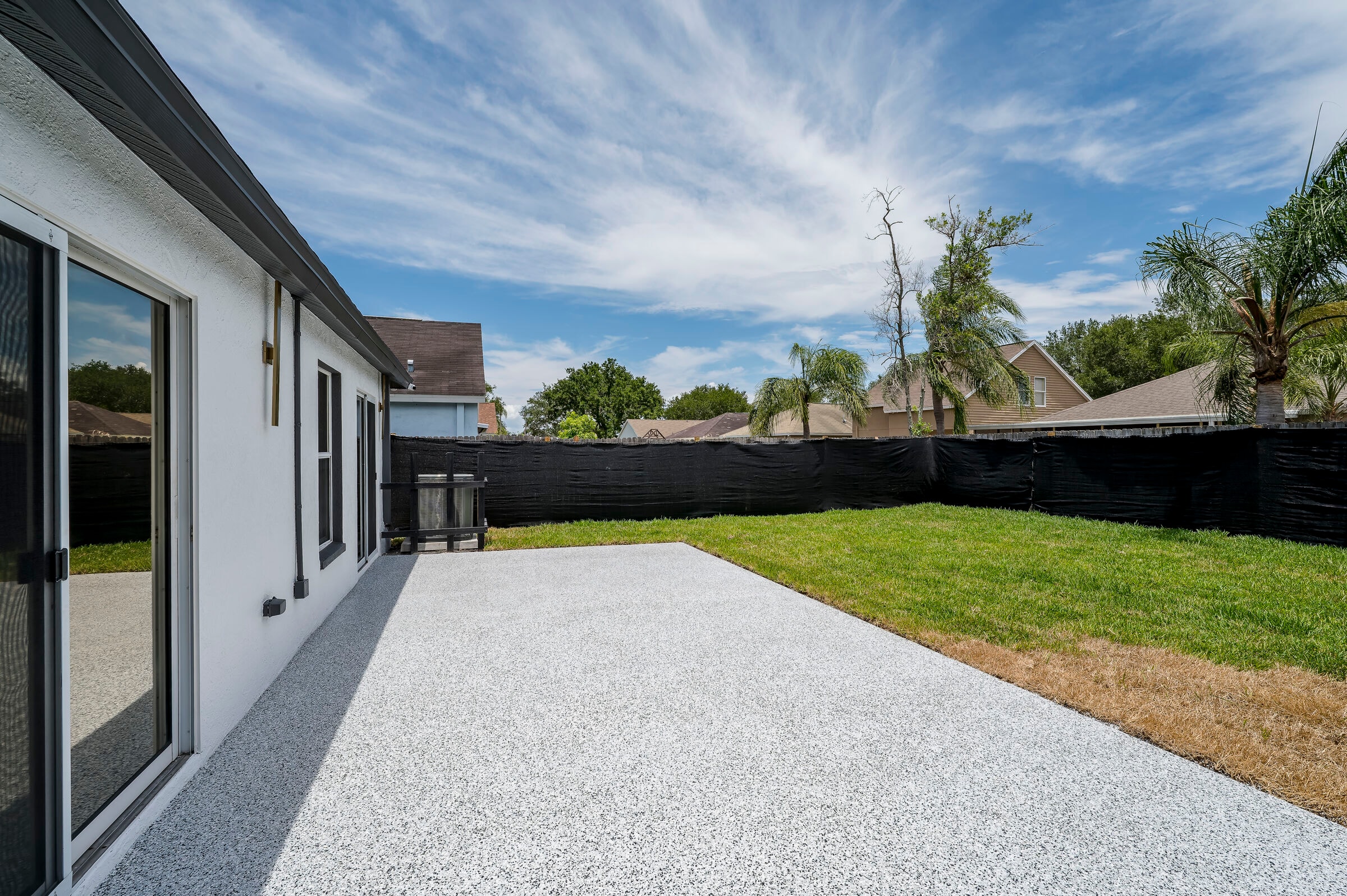 Backyard at 7522 Oxford Garden Circle Apollo Beach Florida — wide view of epoxy patio, green lawn, black privacy fence, and palm trees