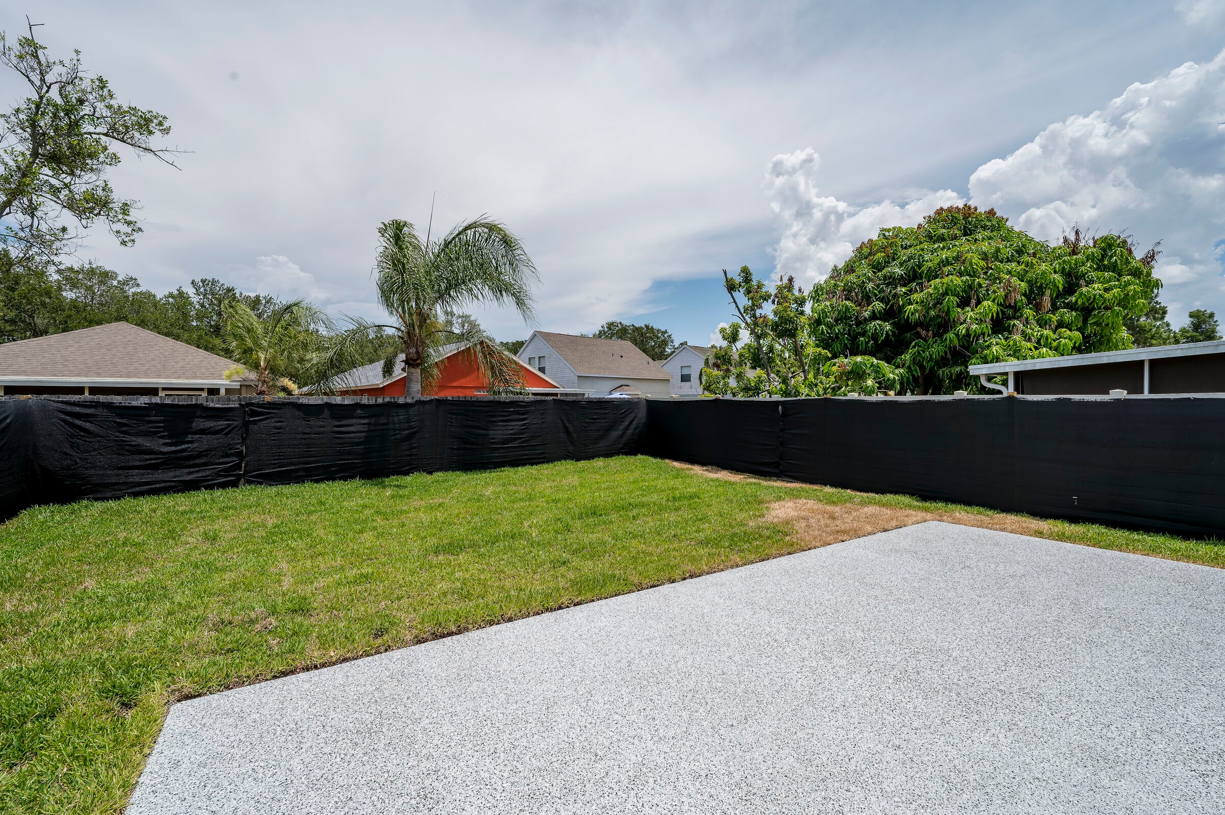 Backyard landscaping at 7522 Oxford Garden Circle in Apollo Beach Florida — epoxy flake patio, green lawn, black privacy fence, and palm tree