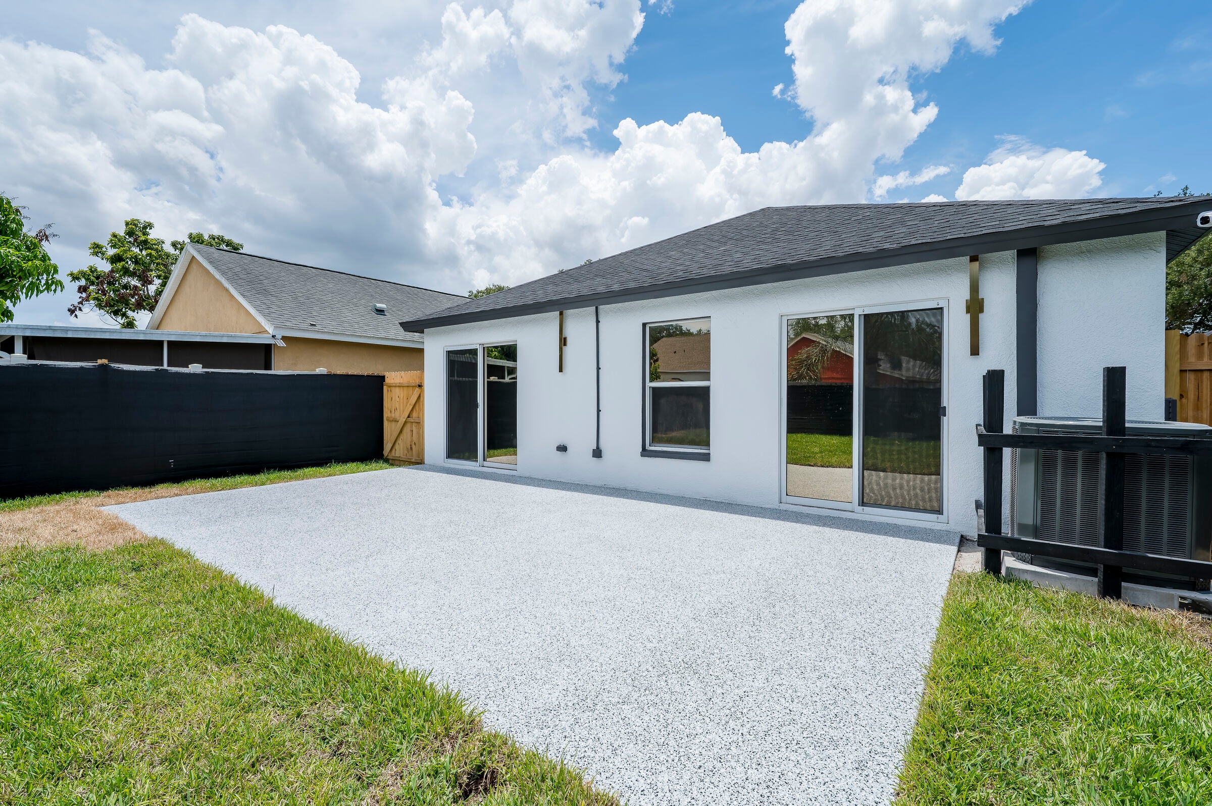 Rear exterior of 7522 Oxford Garden Circle Apollo Beach — white stucco with dark trim, epoxy patio, sliding glass doors, AC units, and black privacy fence